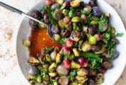 A white bowl filled with sweet and sour brussels sprouts with chestnuts and a serving spoon resting inside.