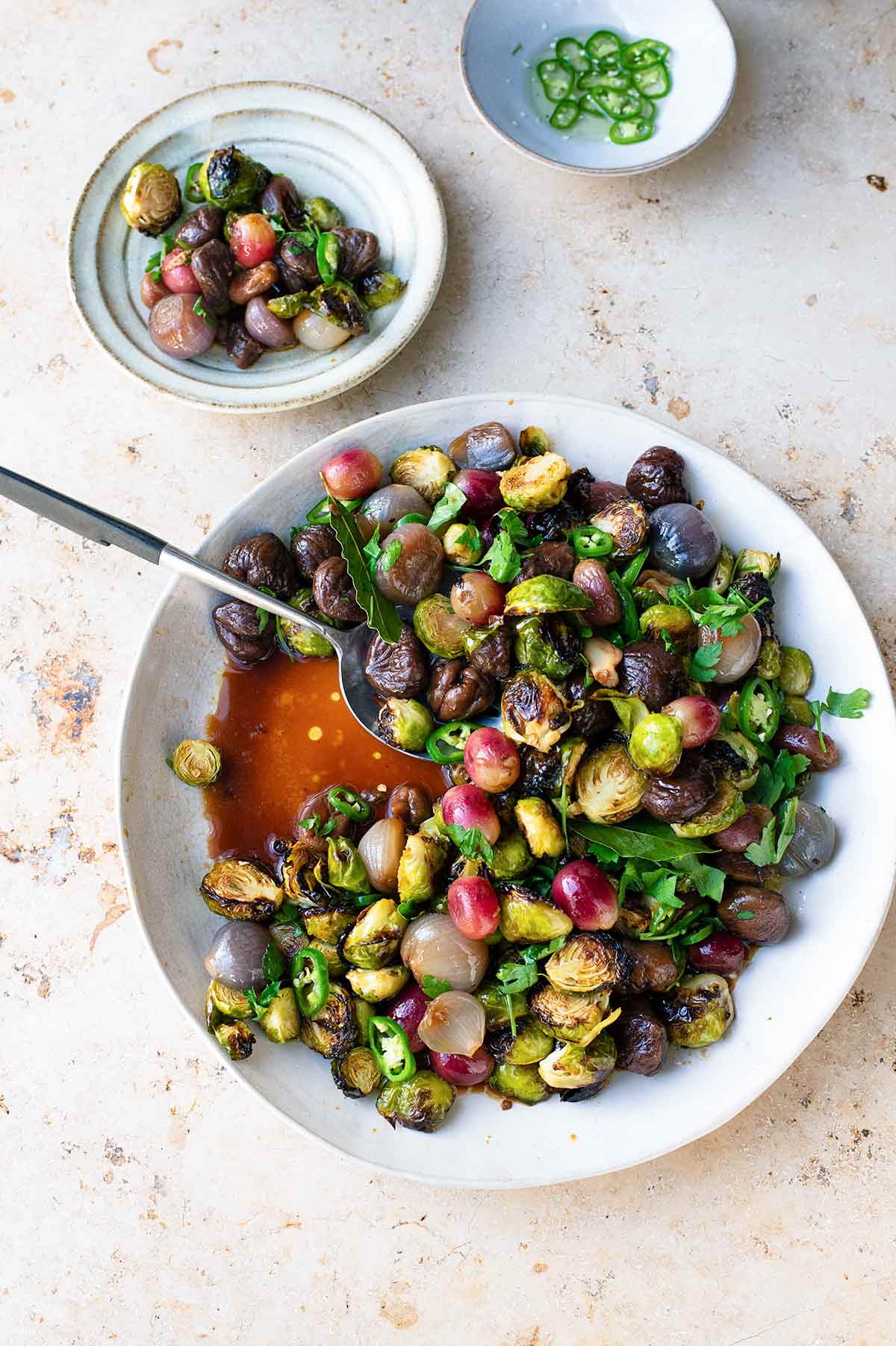 A white bowl filled with sweet and sour brussels sprouts with chestnuts and a serving spoon resting inside.