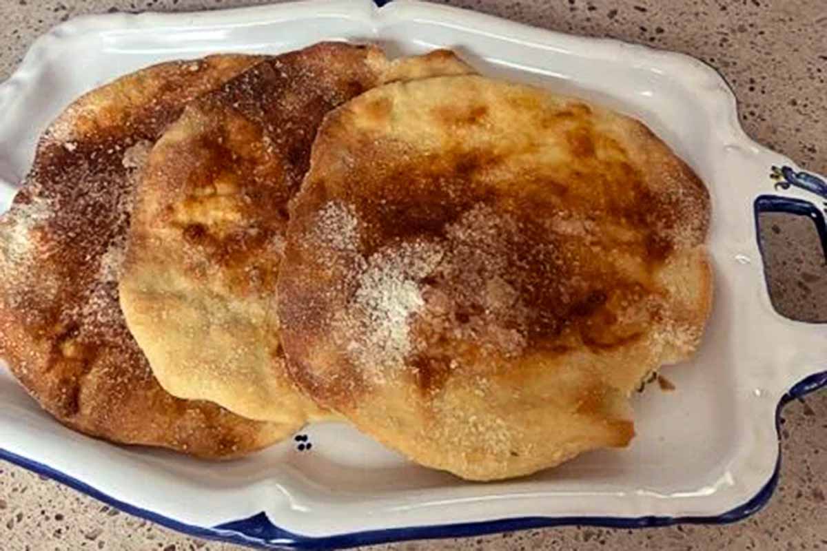 A white plate filled with Spanish tortas (thin biscuits) dusted with sugar.