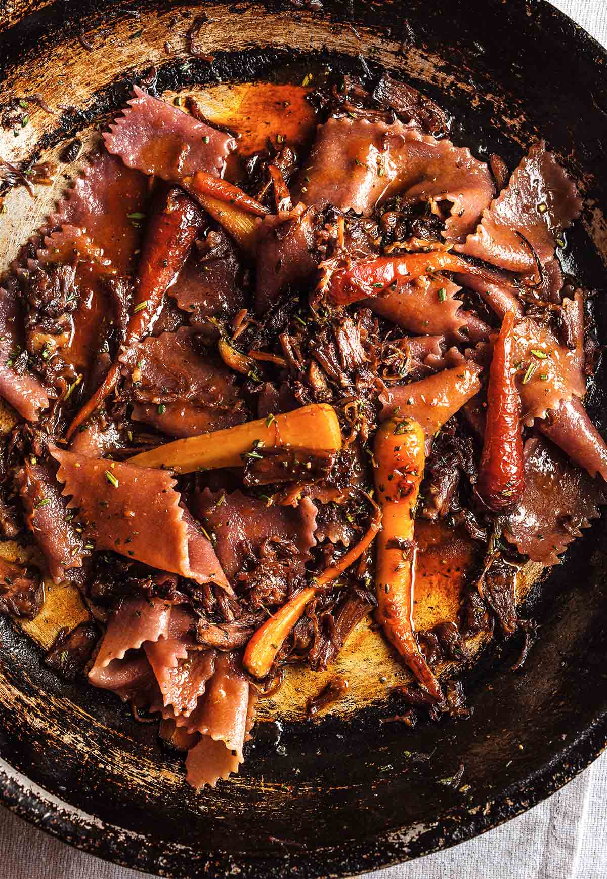 Braised beef with red wine pasta and carrots in a skillet.