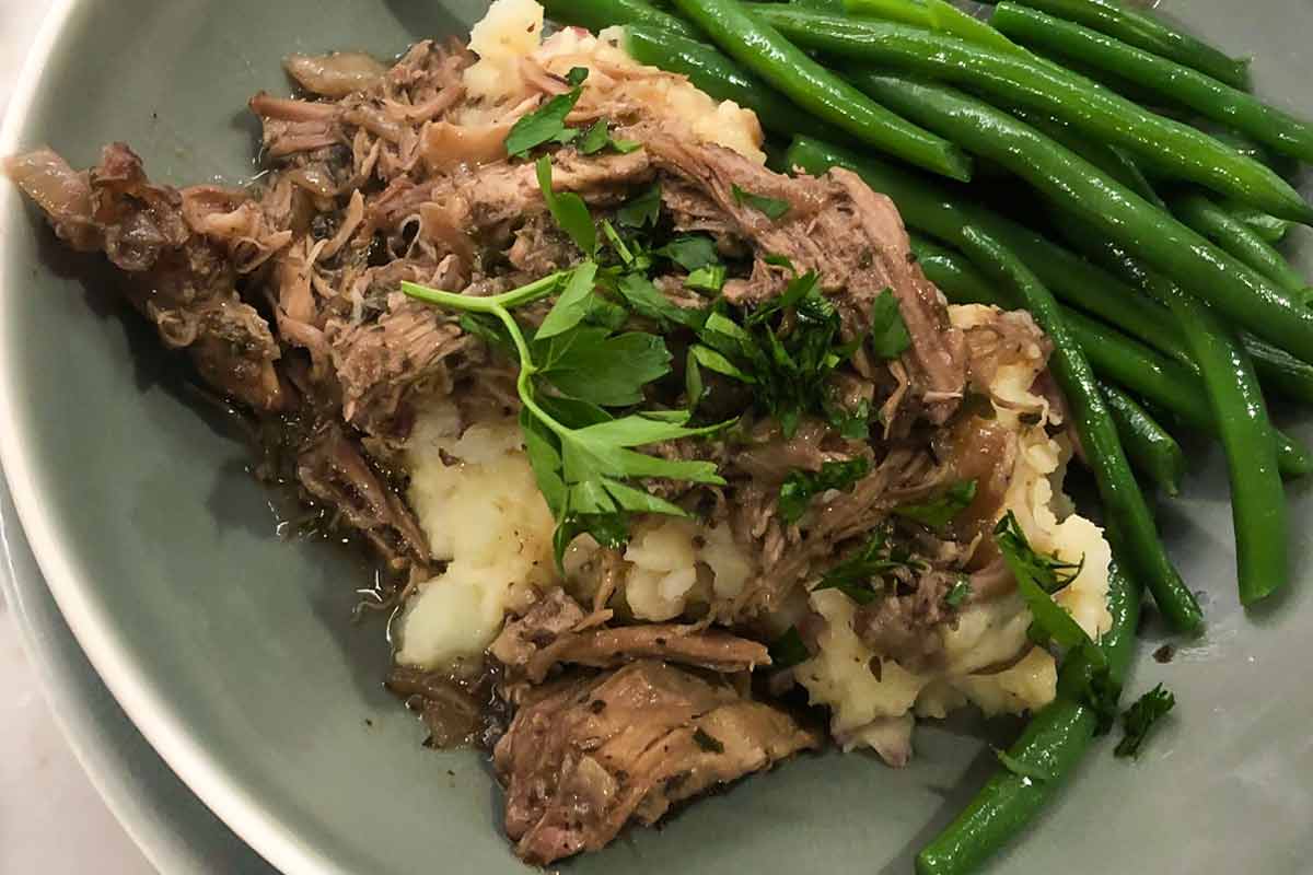 Braised pork with red wine sauce, mashed potatoes, and green beans on a plate.