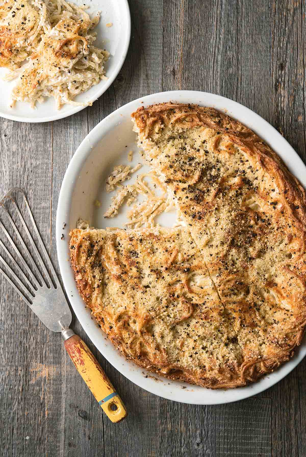 Oval dish with cacio e pepe kugel, a cheese and pepper casserole with fettuccine and ricotta and Pecorino cheeses baked golden