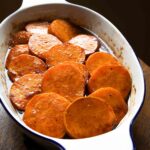 An oval baking dish filled with slices of candied sweet potatoes in a brown sugar syrup.