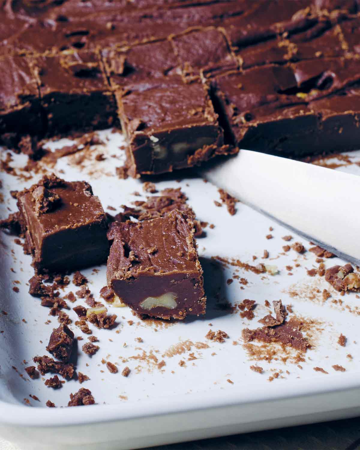 Squares of chocolate fudge on a rimmed baking sheet with a knife resting beside them.