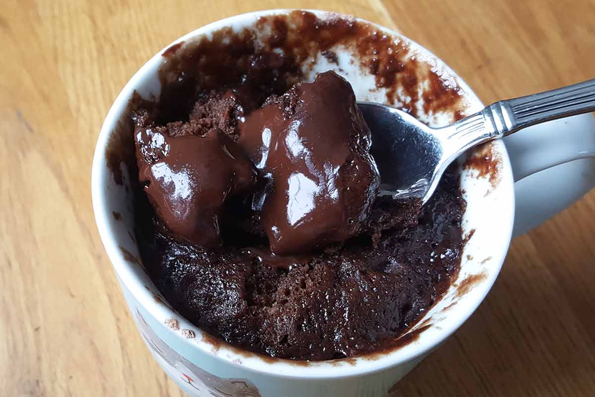 A spoon scooping chocolate mug cake out of a white mug.