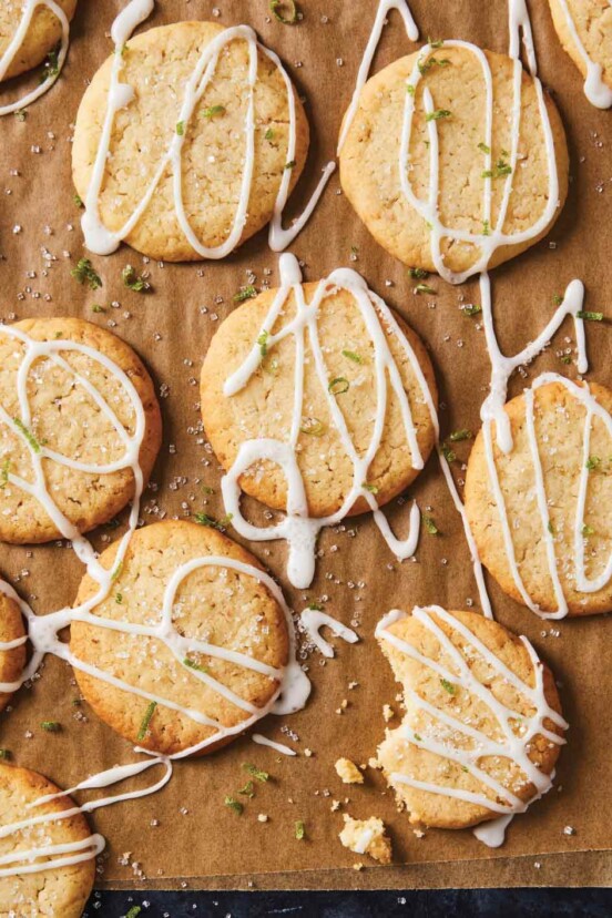 Coconut lime cookies drizzled with icing and garnished with lime zest on wax paper.