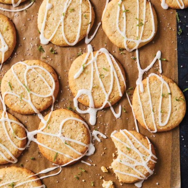 Coconut lime cookies drizzled with icing and garnished with lime zest on wax paper.