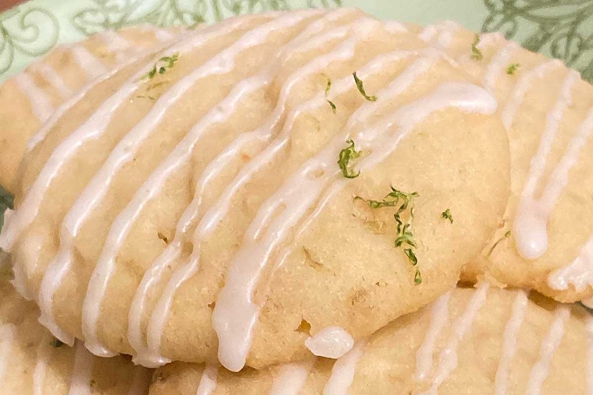 Coconut lime cookies drizzles with icing and topped with lime zest on a green plate.