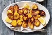 A white plate topped with slices of fried plantains or ndizi kaanga and lemon wedges with a fork on the side.