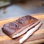 Homemade maple-espresso bacon on a cutting board on a stone slab.