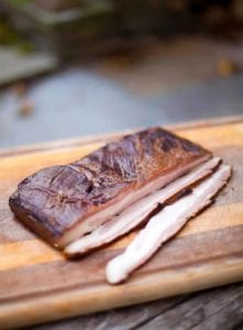 Homemade maple-espresso bacon on a cutting board on a stone slab.