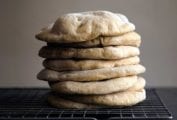 Nine homemade pita bread rounds stacked on a wire rack.