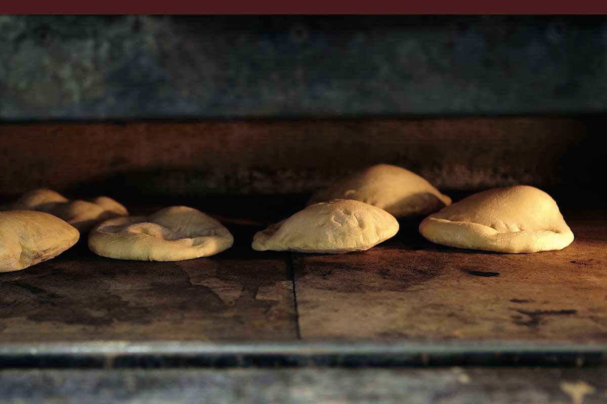 Six homemade pita bread rounds puffing inside an oven.