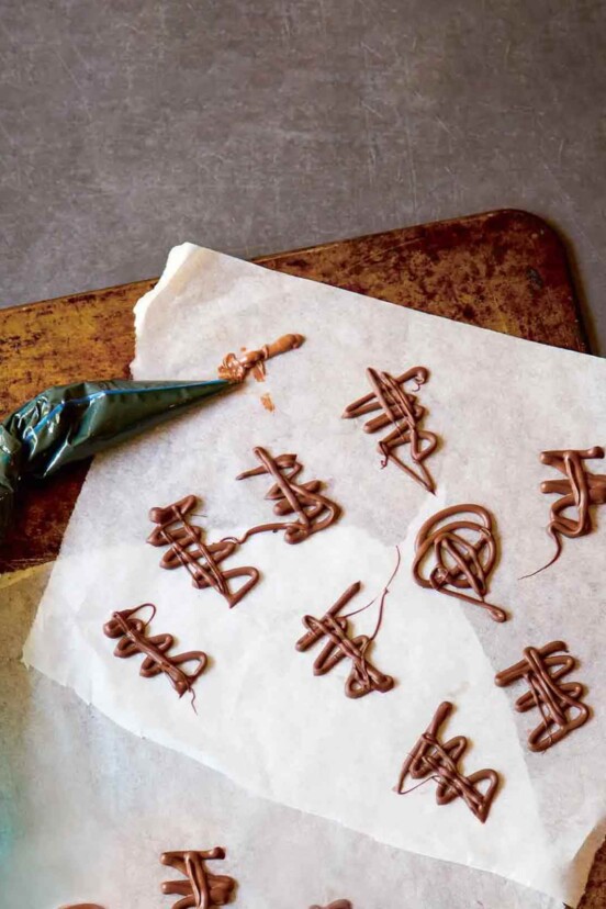 Squiggles of melted chocolate on a piece of parchment with a piping bag lying beside.