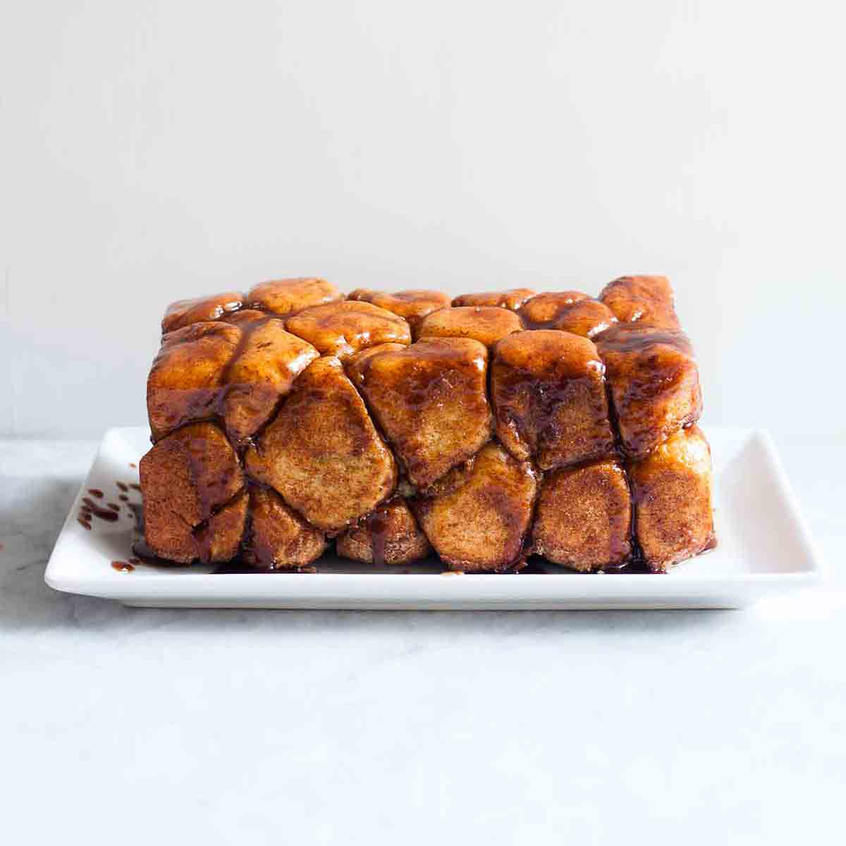 A loaf of monkey bread--balls of caramel-coated bread dough dripping caramel sauce on a rectangle plate