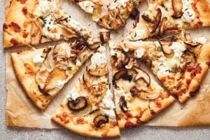 A mushroom pizza with ricotta cut into 8 slices on a piece of browned parchment paper.