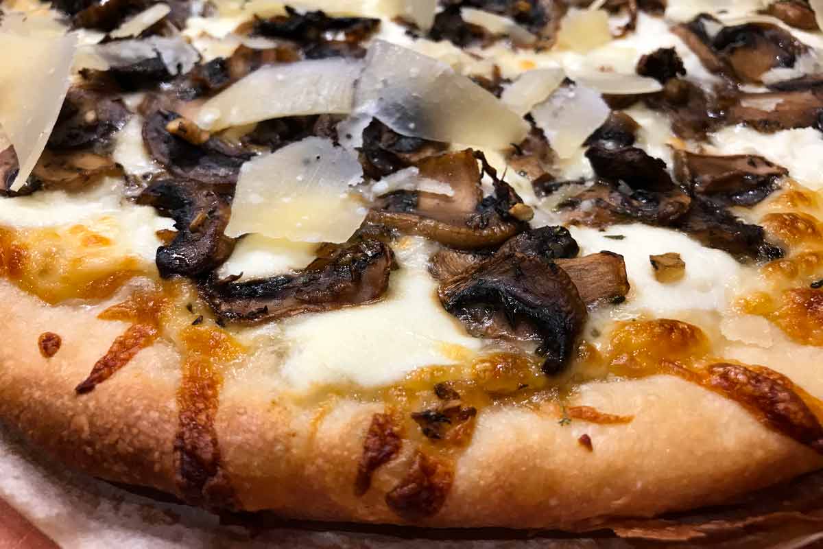 A mushroom pizza with ricotta and shaved parmesan on a sheet of parchment.