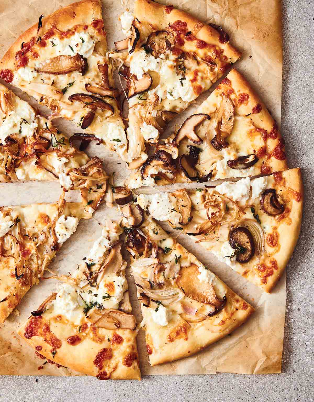 A mushroom pizza with ricotta, cut into 8 slices on a piece of tan parchment paper.