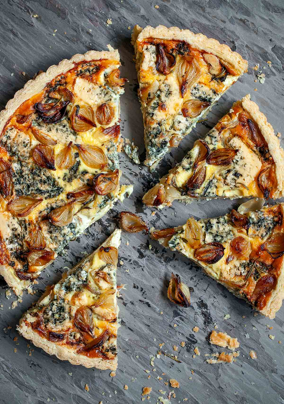 An onion and blue cheese tart cut into wedges with crispy onions scattered around it.