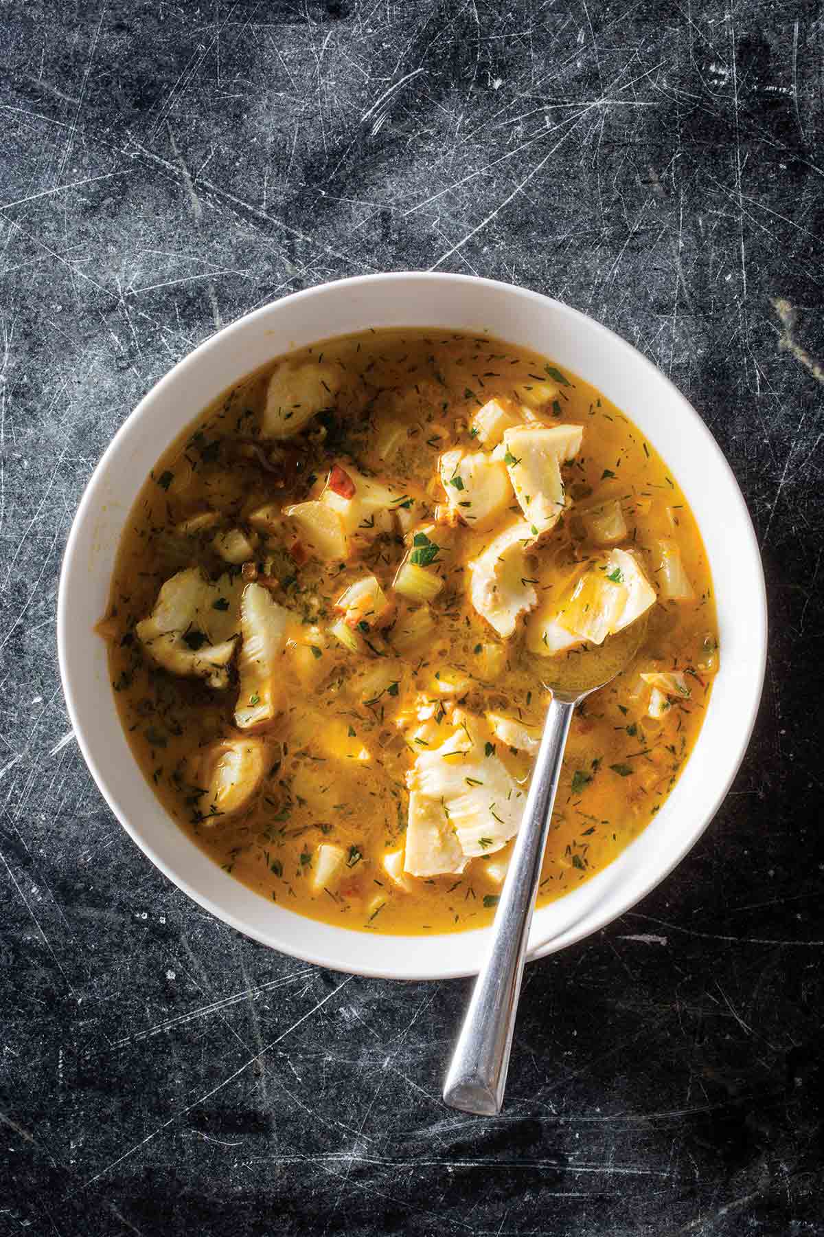 A white bowl filled with Provençale fish soup with a spoon resting inside.