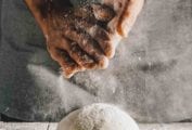 A person dusting flour over a ball of quick pizza dough on a wooden table.