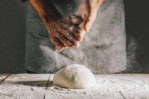 A person dusting flour over a ball of quick pizza dough on a wooden table.