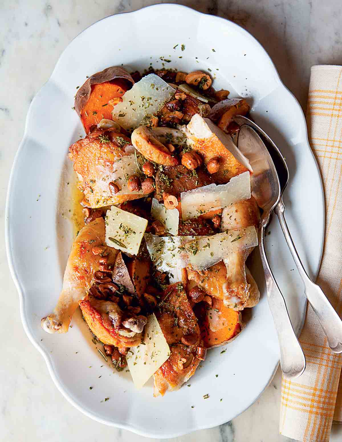 A white platter topped with roast chicken with sweet potatoes and brown butter with two serving spoons and a napkin on the side.