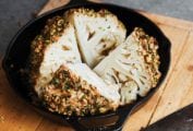 A whole roasted cauliflower with tahini and pistachios cut into four pieces in a cast-iron skillet.