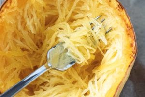A fork scooping strands of roasted spaghetti squash from the center of a halved squash.