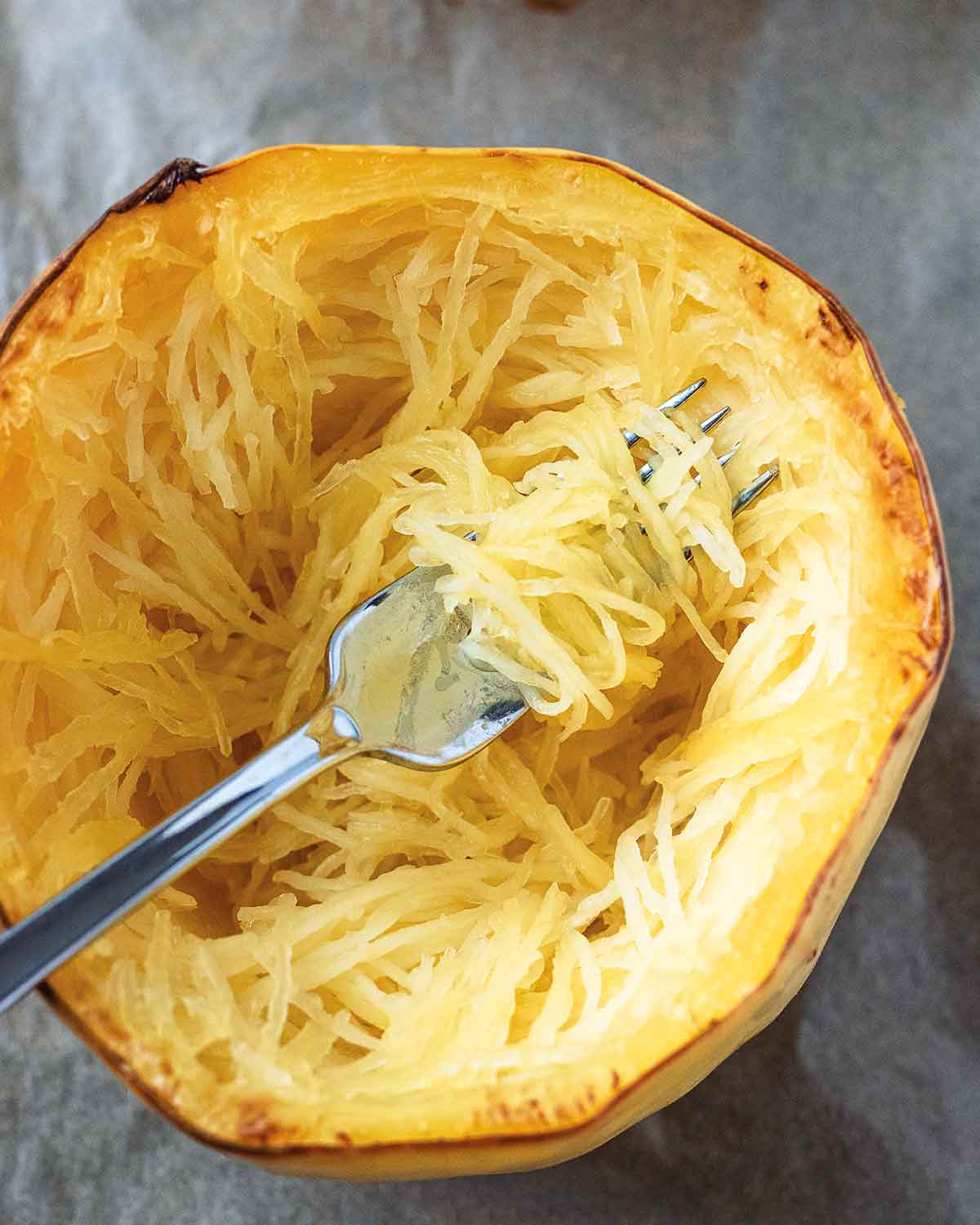 A fork scooping strands of roasted spaghetti squash from the center of a halved squash.