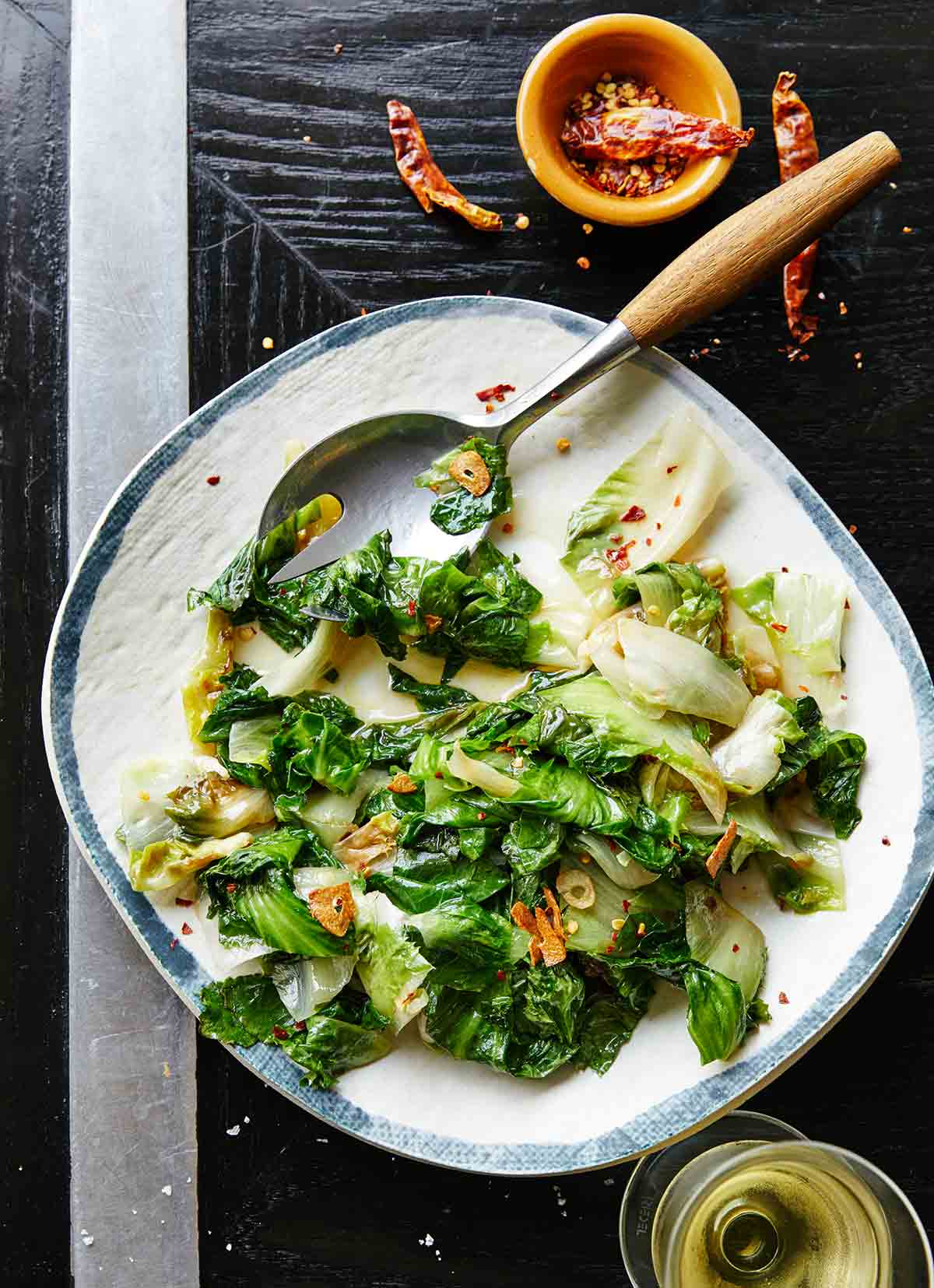 A blue and white serving plate topped with sautéed escarole and a serving spoon on the side.