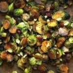 Spicy roasted Brussels sprouts with dried cranberries and macadamia nuts on a baking sheet.