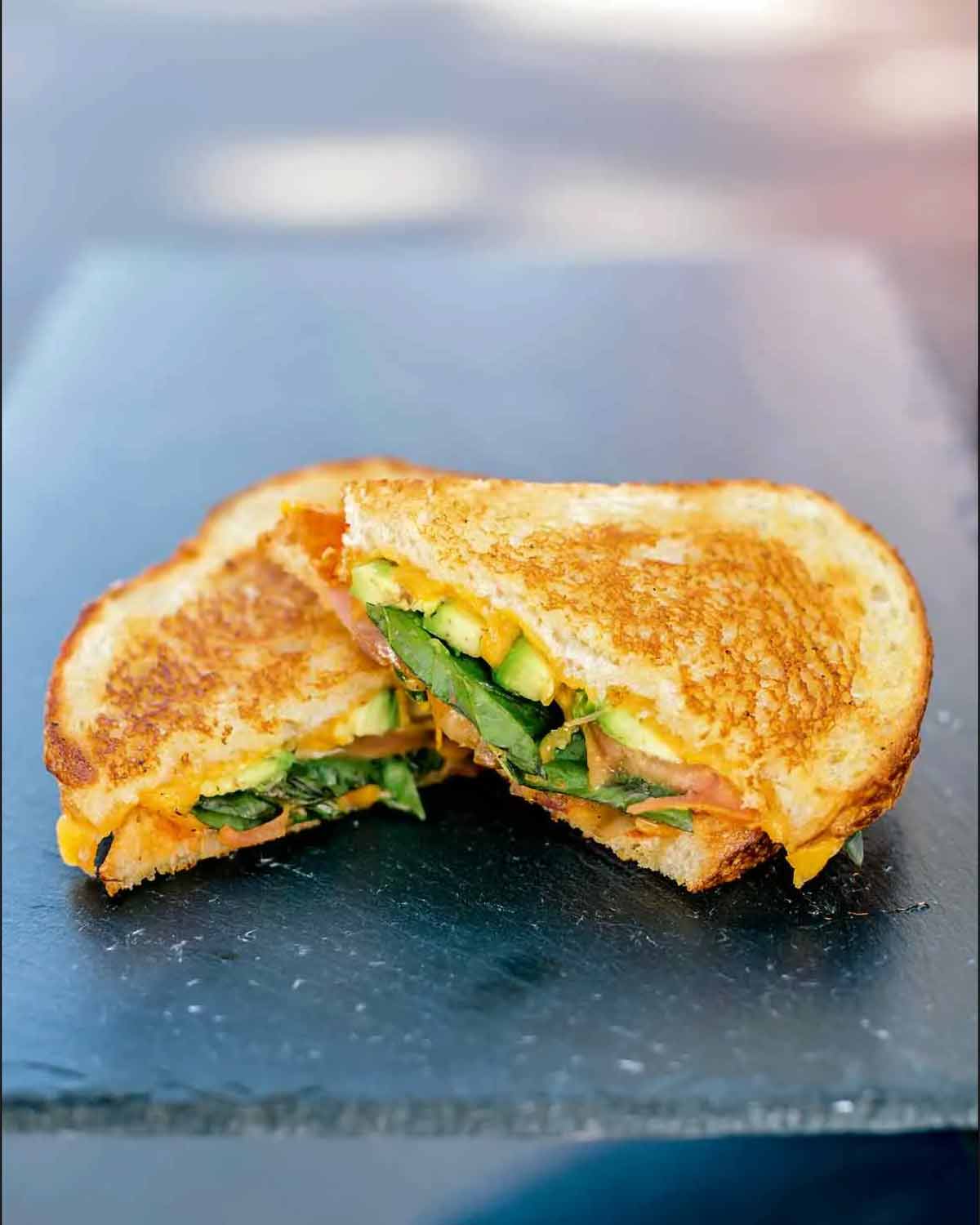 A veggie grilled cheese sandwich sliced in half on a glass platter