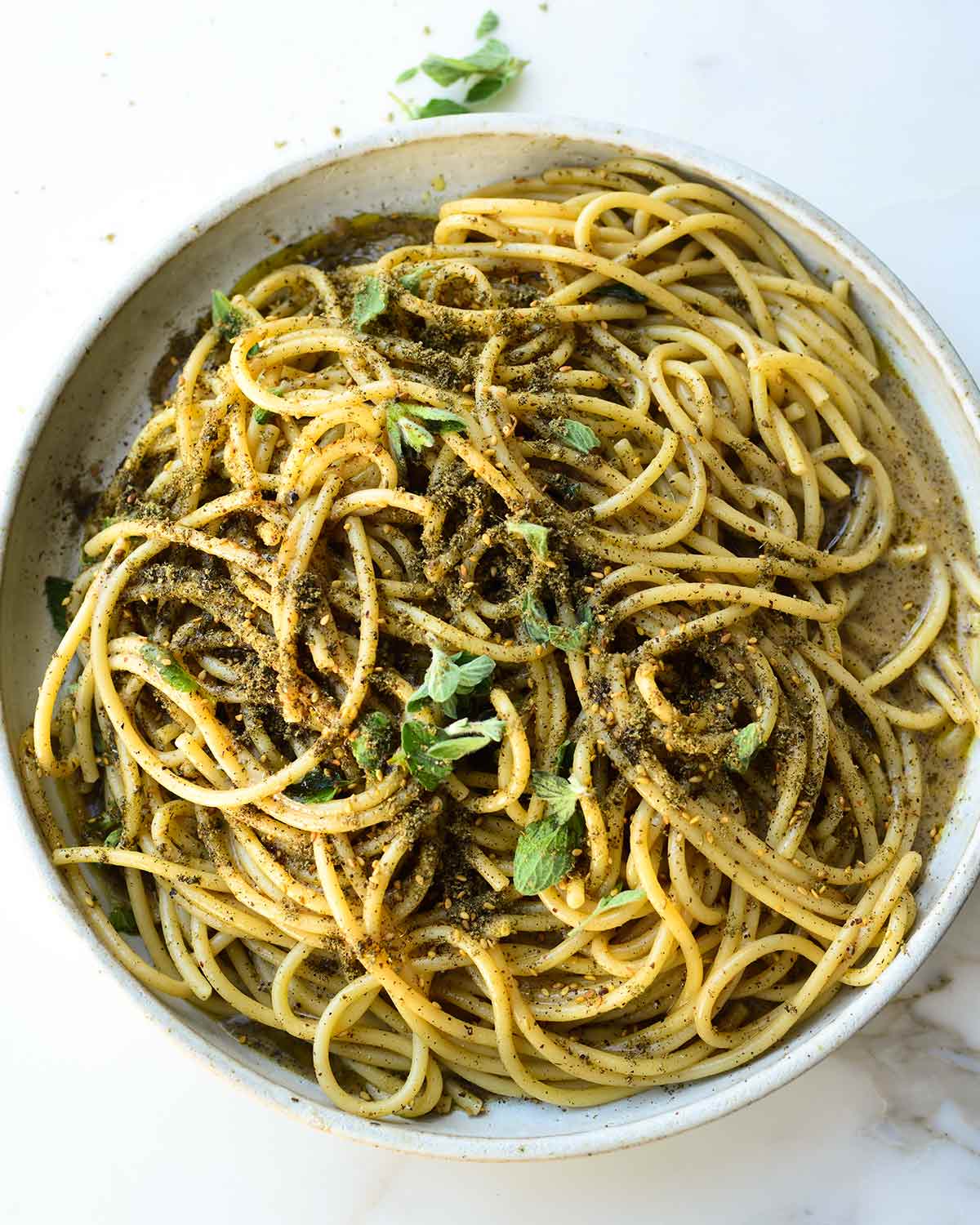 A ceramic bowl filled with za'atar cacio e pepe and topped with fresh marjoram leaves.