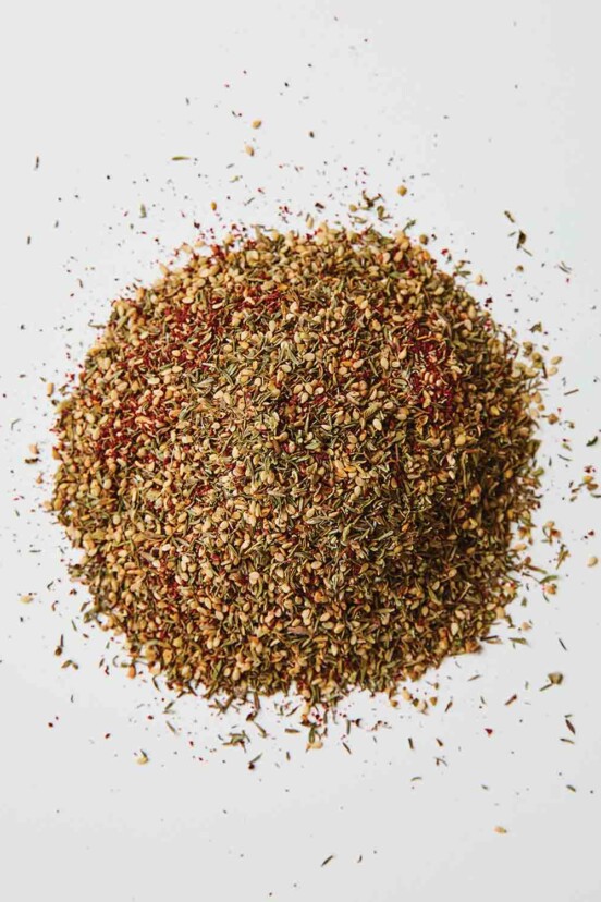 A scoop of za'atar spice blend on a white background.
