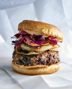 A black bean mushroom burger topped with onions, sauce, and purple leaves.