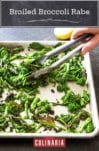 Pieces of broiled broccoli rabe being turned over on a sheet pan by a person using tongs.