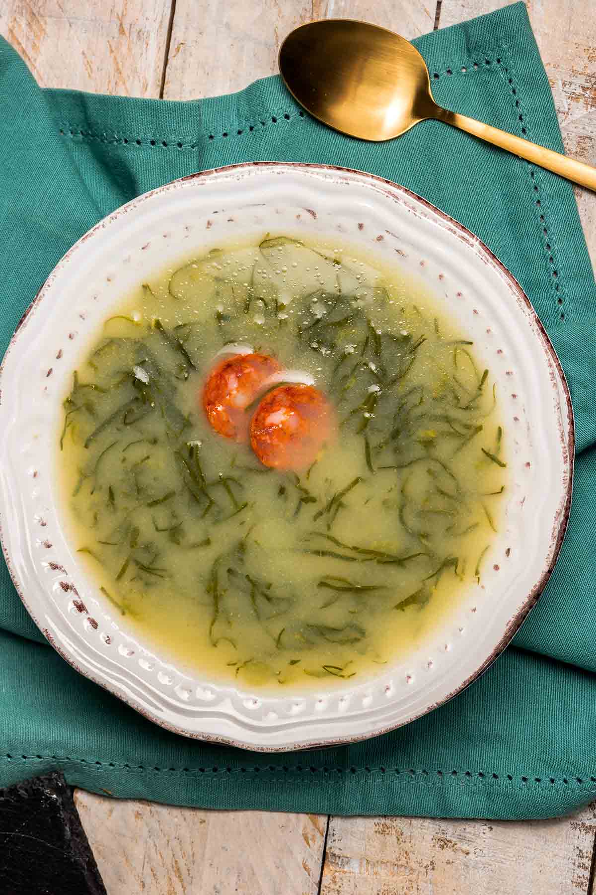 A white bowl of caldo verde, or Portuguese kale soup with thinly sliced kale and a single chorizo coin floating in the center.