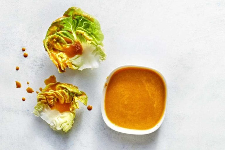 A small cup of carrot ginger dressing with some drizzled over two pieces of lettuce lying beside it.