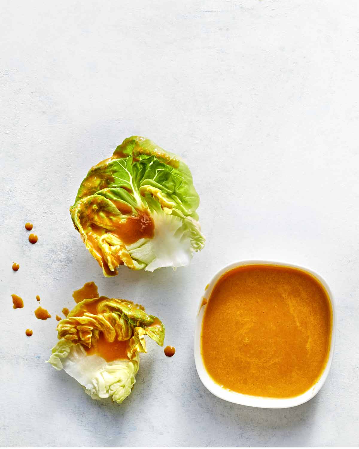 A small cup of carrot ginger dressing with some drizzled over two pieces of lettuce lying beside it.