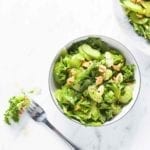 A small and large bowl of celery salad topped with nuts and a fork resting beside them.