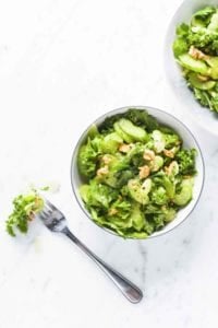 A small and large bowl of celery salad topped with nuts and a fork resting beside them.