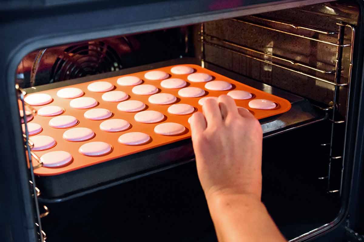 Someone putting a baking sheet filled with macarons into the convection oven.