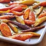 Colorful curried roasted carrots scattered on a rimmed sheet pan.