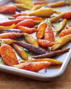 Colorful curried roasted carrots scattered on a rimmed sheet pan.