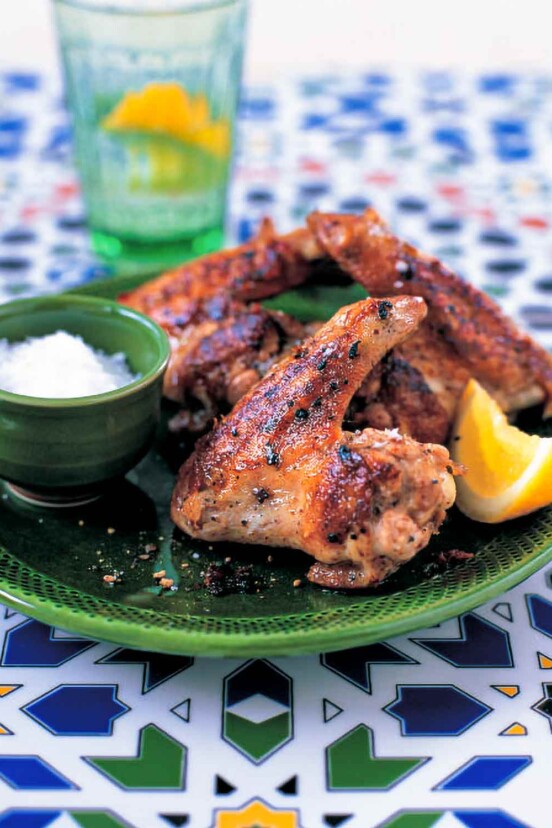 A green plate topped with a few garlicky chicken wings, a bowl of salt, and a lemon wedge.
