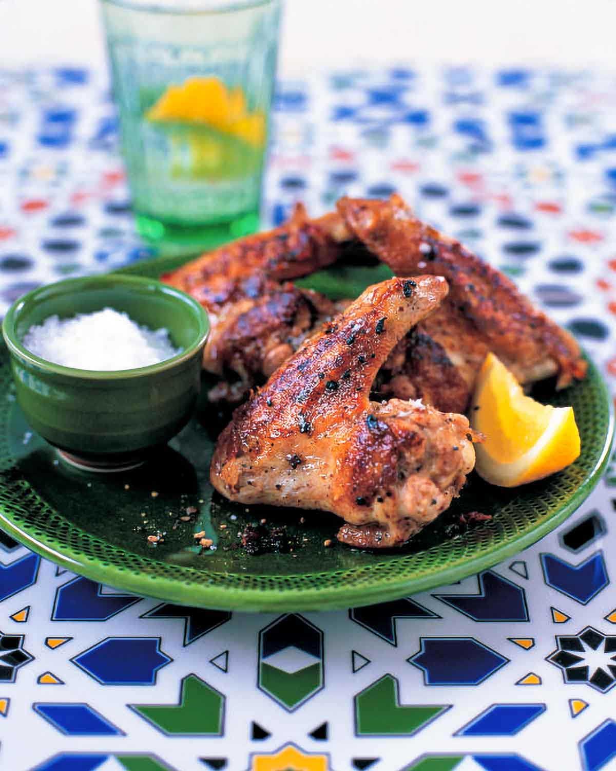 A green plate topped with a few garlicky chicken wings, a bowl of salt, and a lemon wedge.