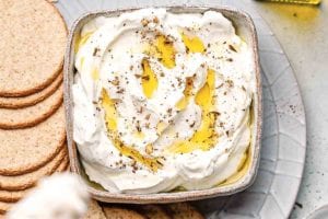 A bowl of homemade labneh with za'atar drizzled with olive oil on a platter with crackers.
