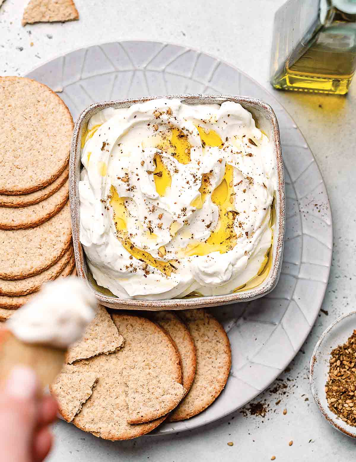 A bowl of homemade labneh with za'atar drizzled with olive oil on a platter with crackers.