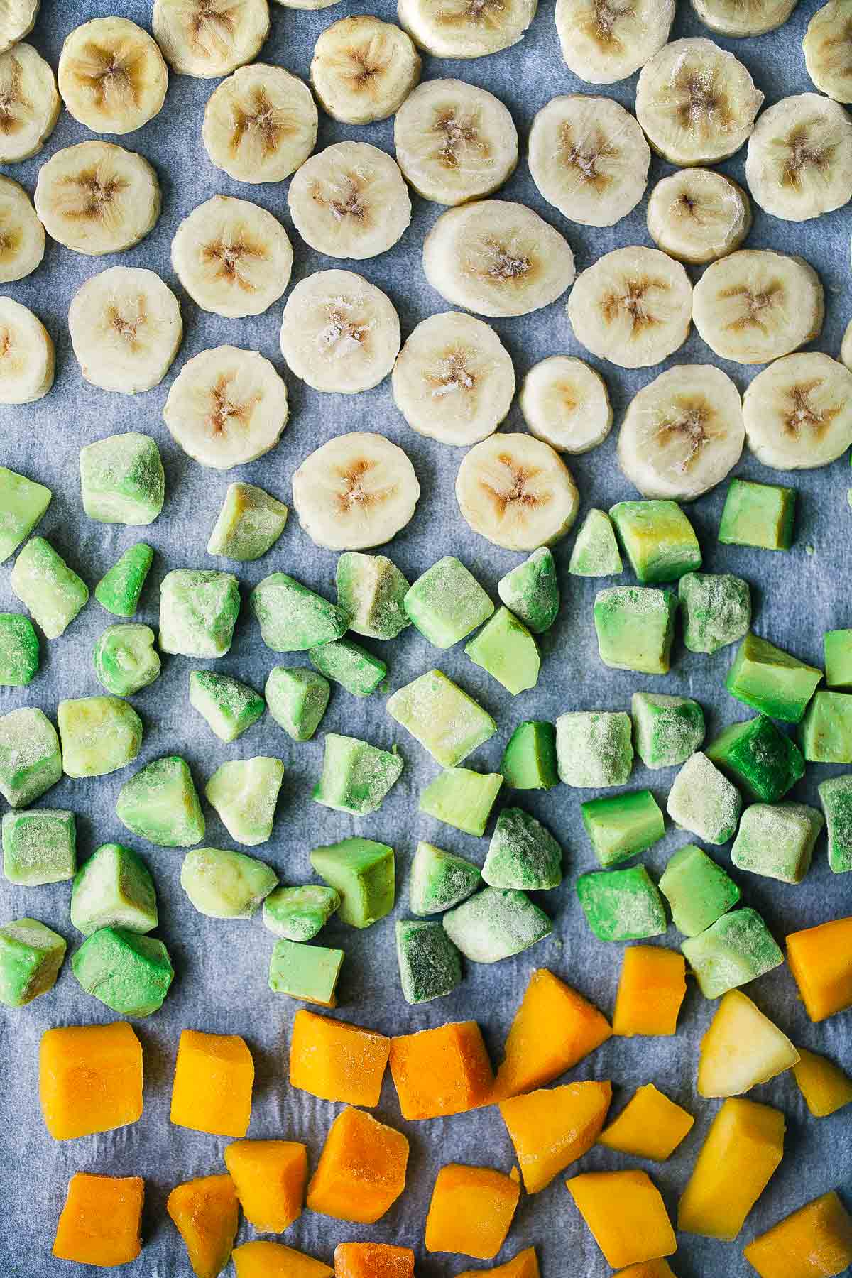 A baking sheet filled with frozen banana, avocado, and mango, using the method of how to freeze bananas.
